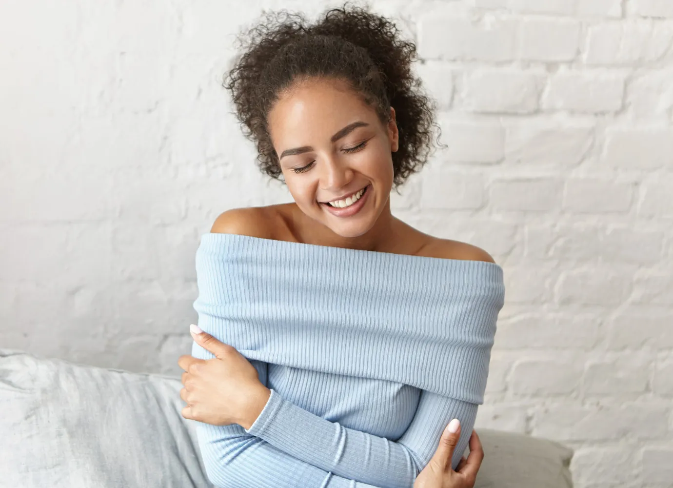 Mulher sorridente, de olhos fechados, abraçando a si mesma com tranquilidade